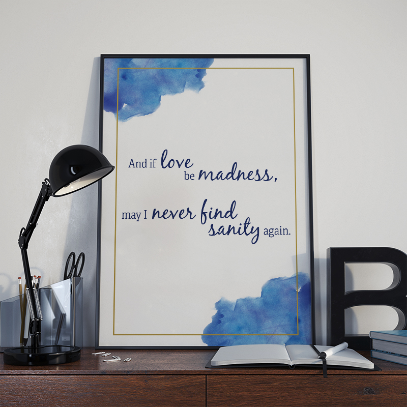 framed white poster with gold border and blue watercolor splotches reading 'and if love be madness may i never find sanity again' set on a desk scene